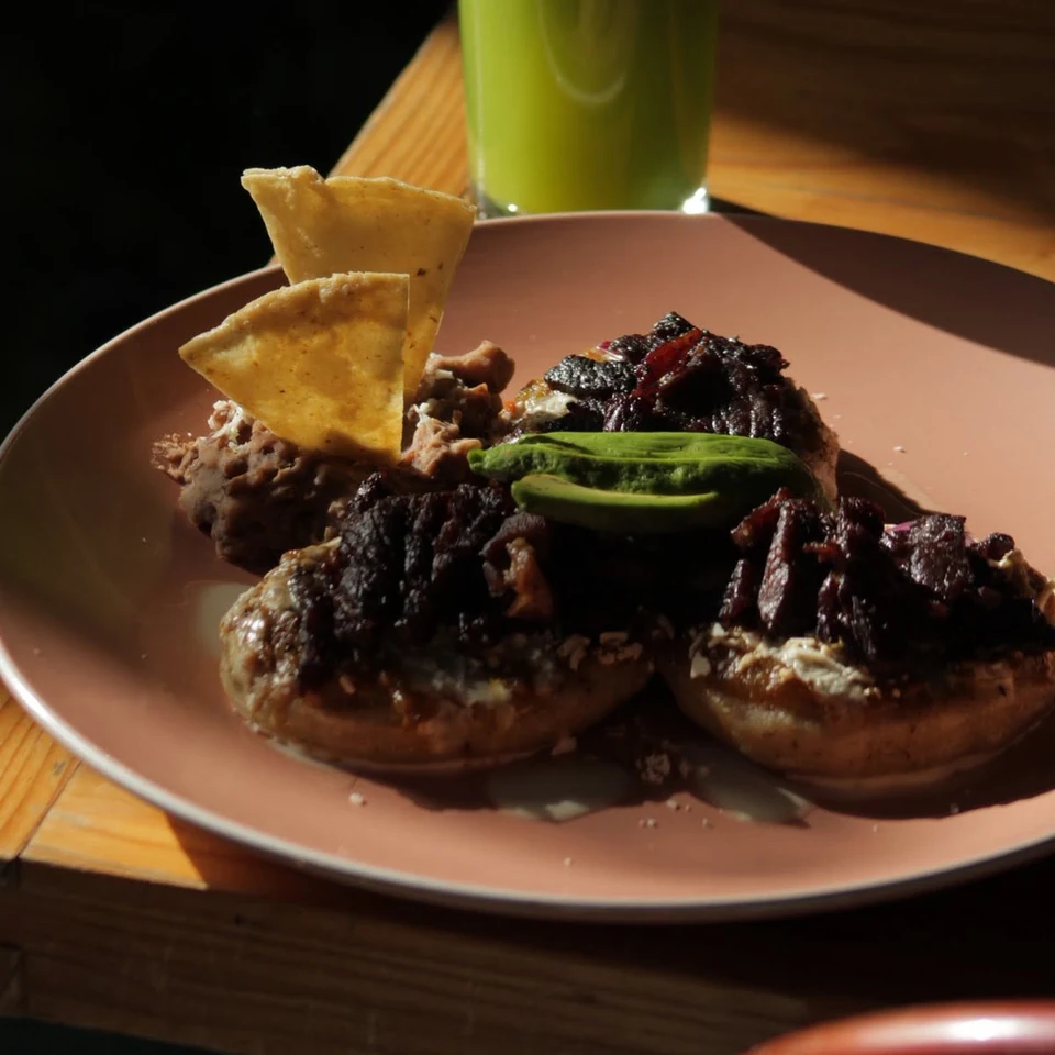 Plato con tres tlayoyos coronados con carne, aguacate y frijoles refritos, junto a un vaso de jugo verde