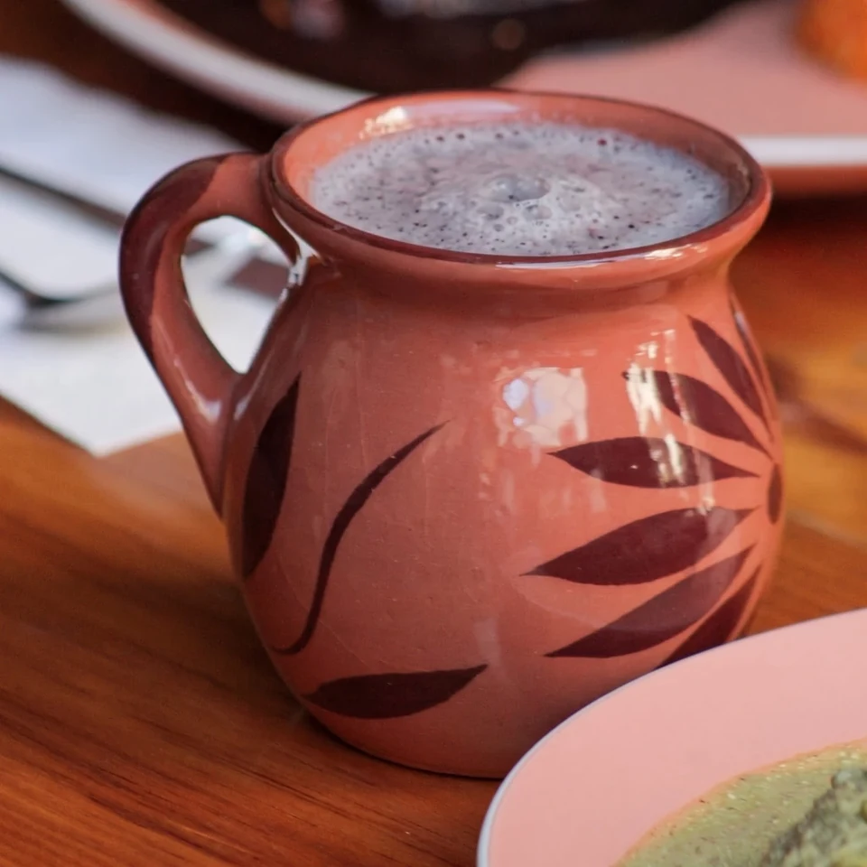 Jarrito de barro con atole espumoso sobre una mesa de madera